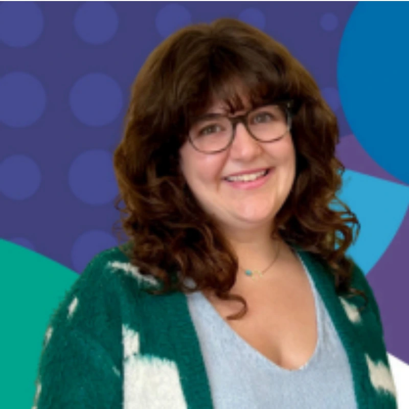 Smiling person with curly hair and glasses against a colourful geometric background, wearing a green and white cardigan and blue top.